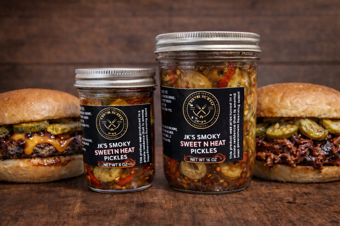 JK’s BBQ Pit Smoky Sweet N Heat Pickles in 8 oz and 16 oz jars on a rustic wooden table with a cheeseburger and BBQ pulled pork sandwich topped with pickles.