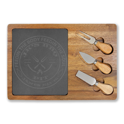 Wooden cutting board with slate surface and three cheese knives on a white background