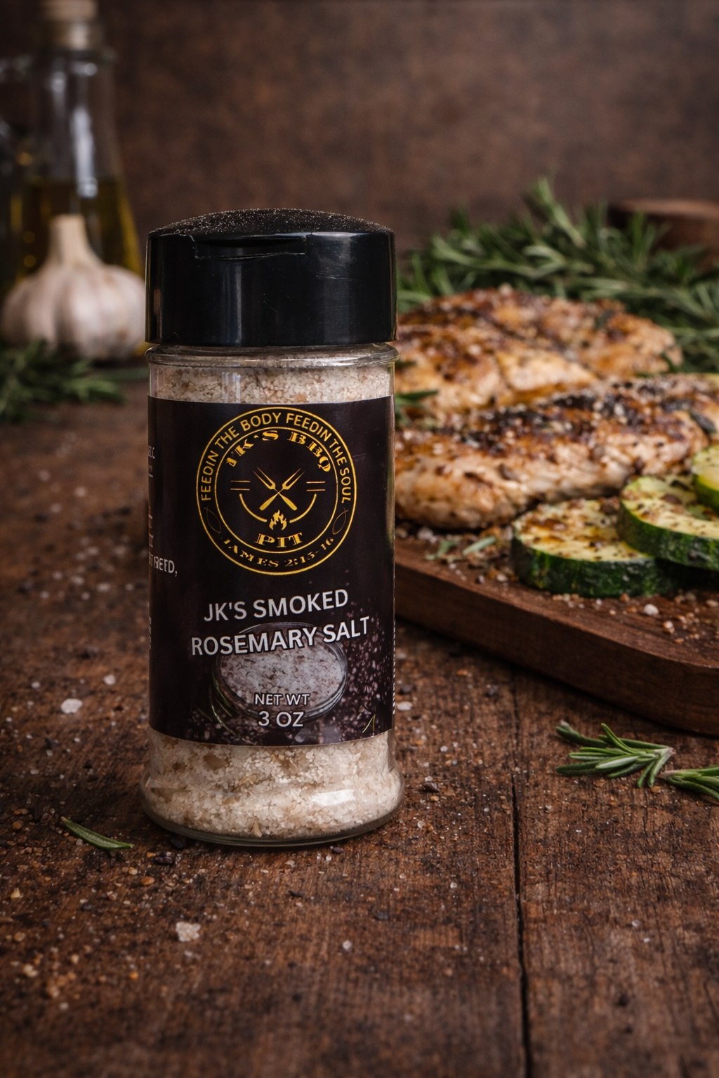 Smoked rosemary salt seasoning by JK's BBQ Pit with grilled chicken and zucchini on a rustic wooden table.