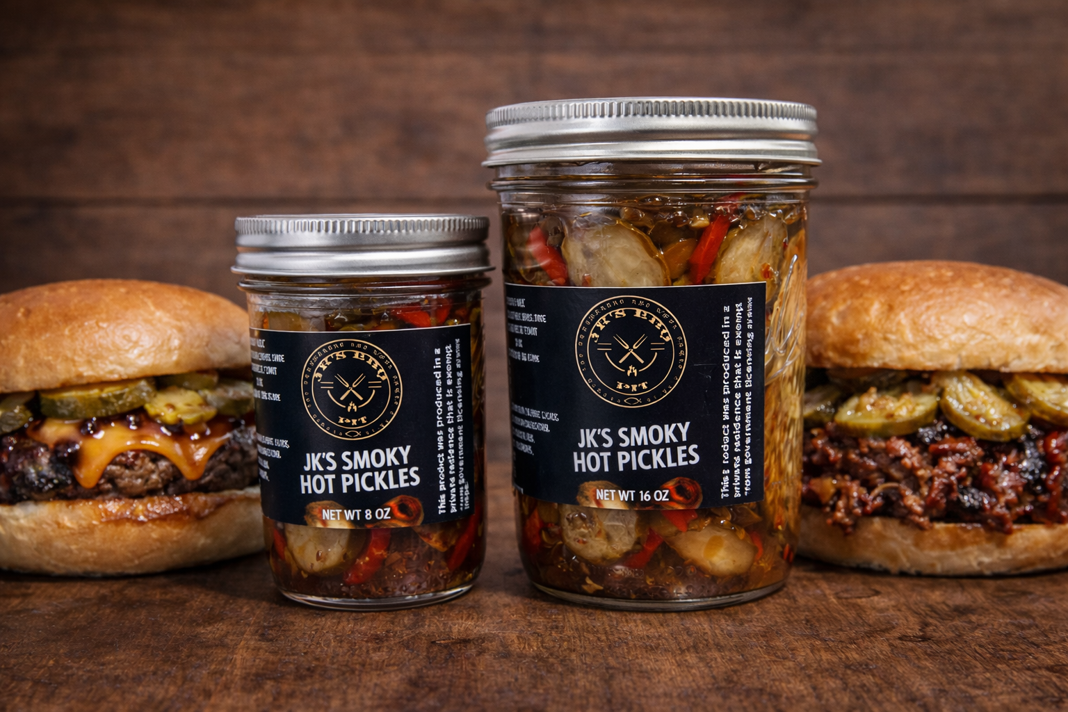 JK’s BBQ Pit Smoky Hot Pickles in 8 oz and 16 oz glass jars on a rustic wooden table with a cheeseburger and BBQ pulled pork sandwich topped with pickles.