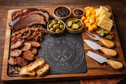 BBQ charcuterie board with brisket, sausage, smoked cheeses, olives, and pickles on JK’s BBQ Pit engraved acacia slate serving board