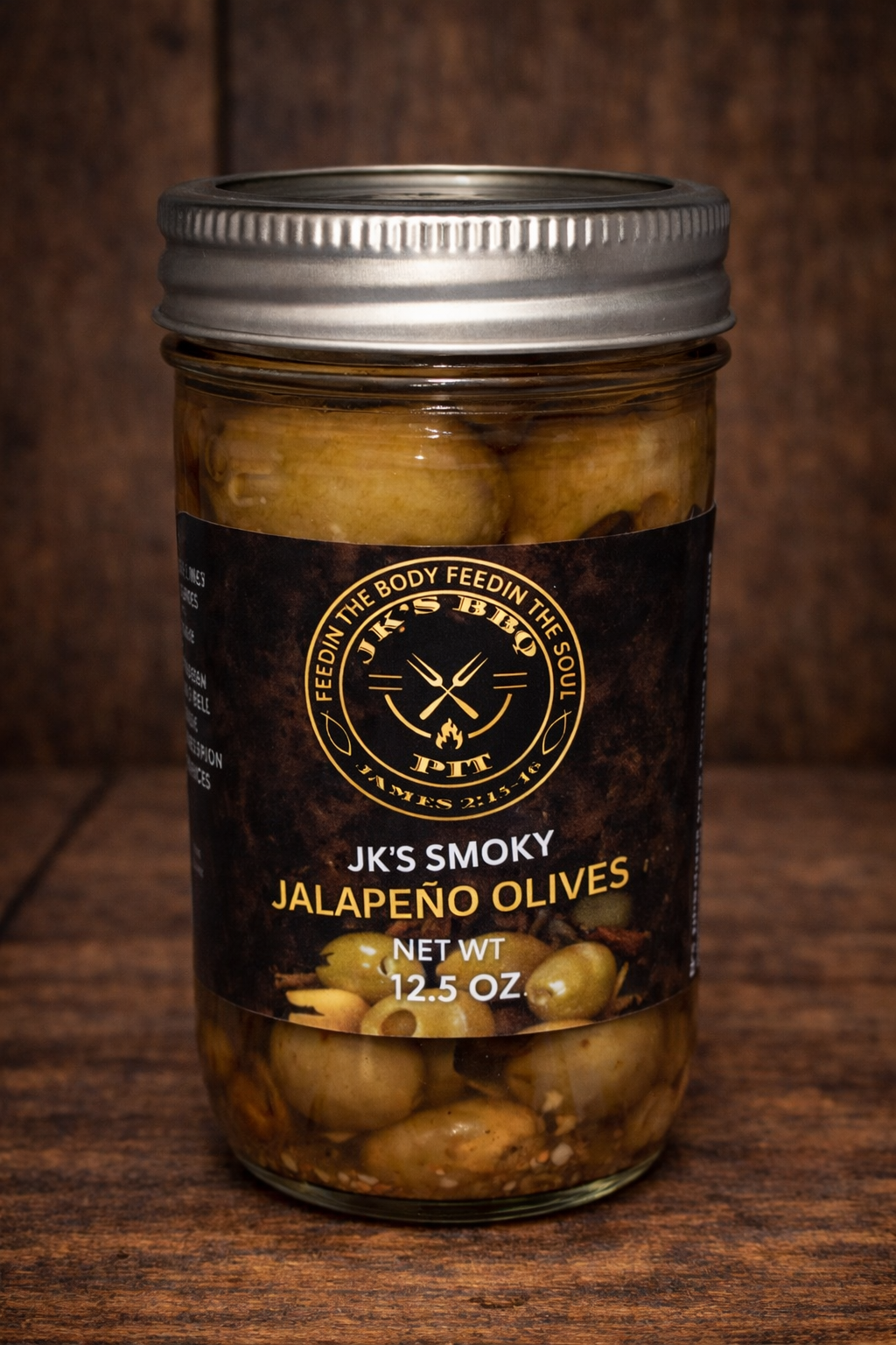 JK's BBQ Pit Smoky Jalapeño Olives in a 12.5 oz mason jar with black and gold label on a rustic wooden background