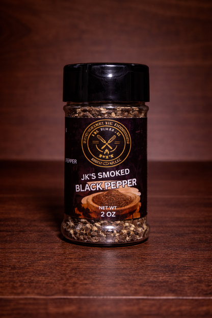 JK’s Smoked Black Pepper 2 oz bottle on wooden background with coarse cracked pepper visible in clear seasoning jar