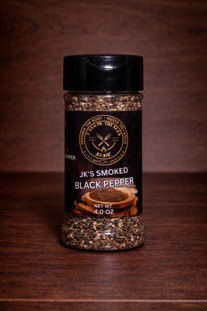 JK’s Smoked Black Pepper 4 oz bottle on wooden background with coarse cracked pepper visible in clear seasoning jar