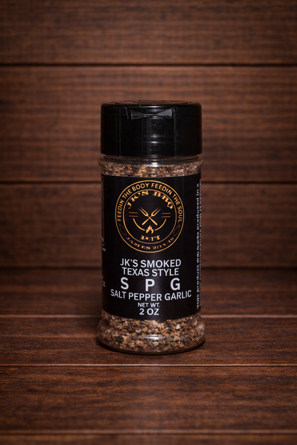 JK's Smoked Texas Style SPG seasoning 2 oz bottle on dark rustic wooden table and wood wall background – salt pepper garlic BBQ rub for brisket, steak, and grilling