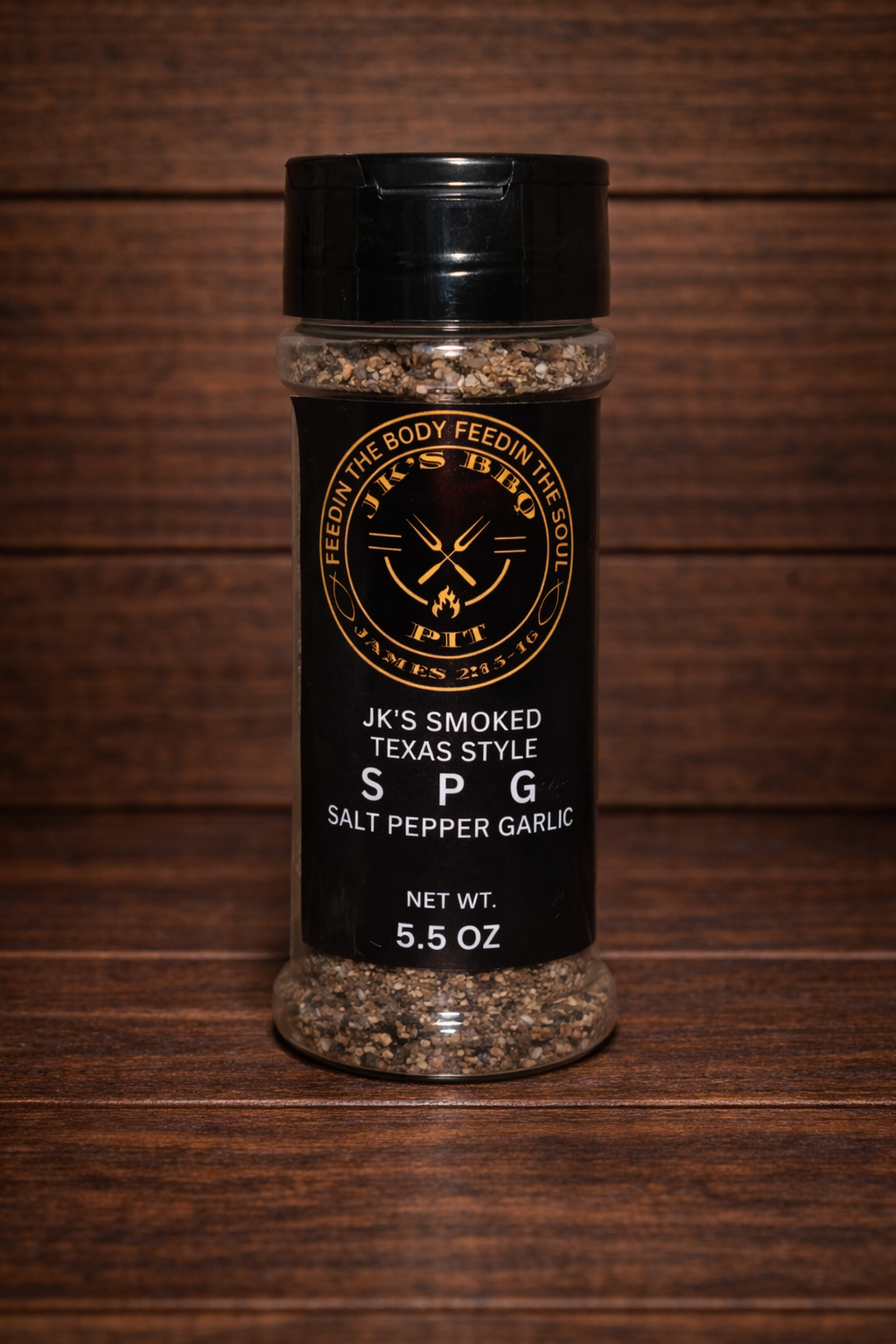 JK's Smoked Texas Style SPG seasoning (salt pepper garlic) 5.5 oz bottle on dark rustic wooden table and wood wall background – Texas style BBQ rub for brisket, steak, and grilling